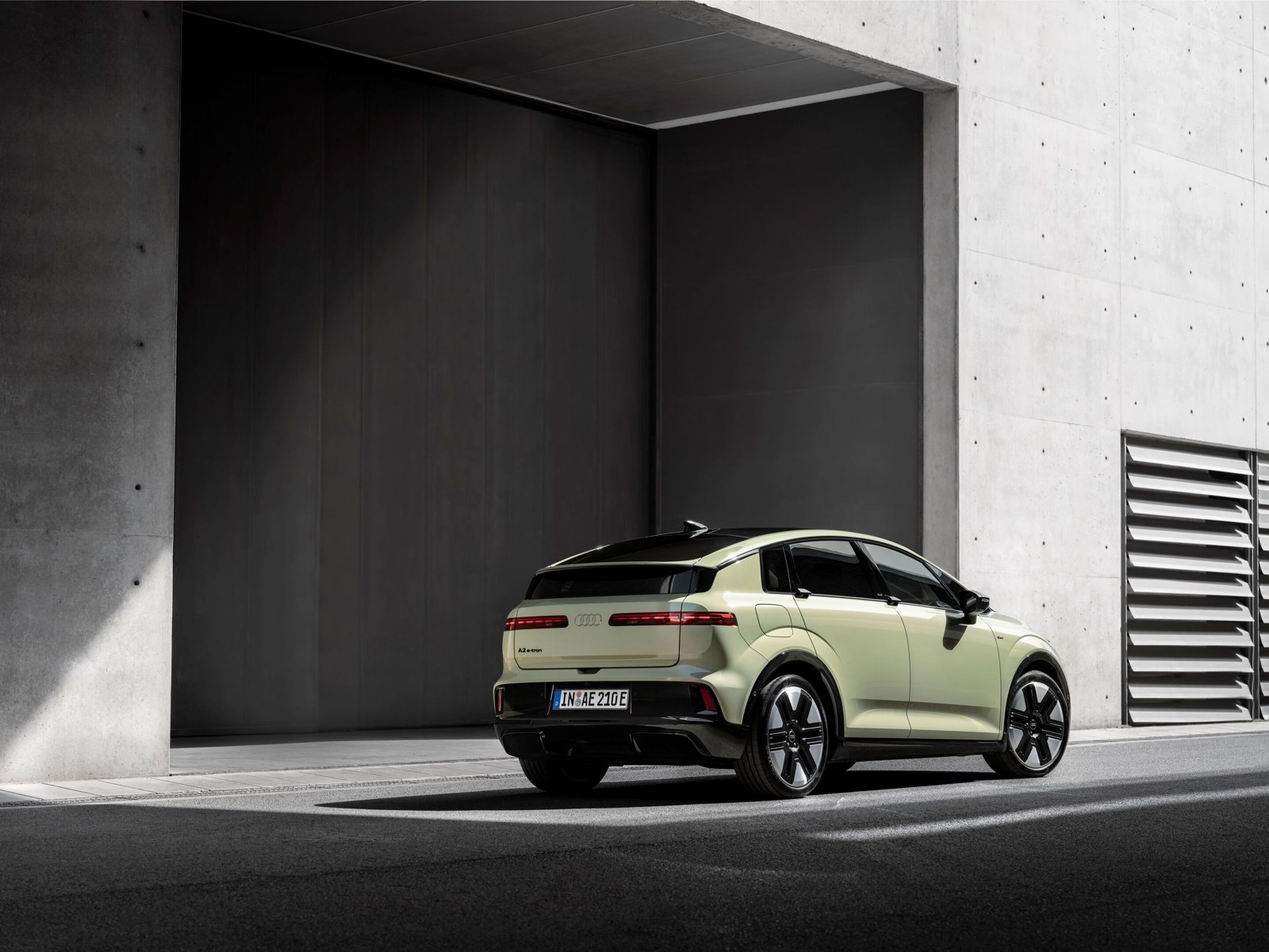 Pistachegroene Audi A2 e-tron van schuin achteren bij een betonnen gebouw.